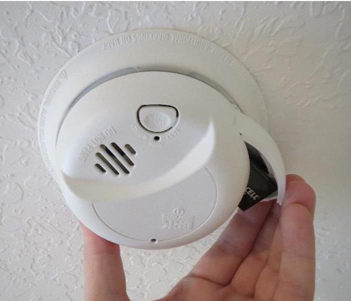 close view of hand opening battery door on a ceiling smoke alarm