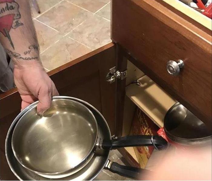 Hand pulling a pan out of a lower kitchen cabinet 